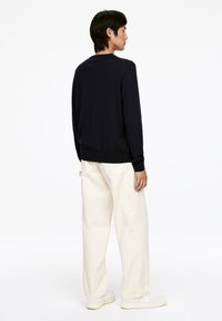 Navy-blaues, gestricktes Langarm-Sweatshirt mit gerippten Bündchen und Saum, kombiniert mit weißen, locker sitzenden Cargo-Hosen und weißen Sneakers.