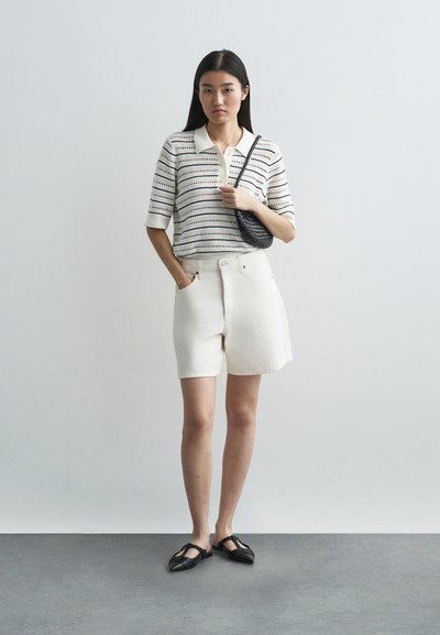 Λευκές κοντές τζιν βερμούδες, πλεκτό πουκάμισο με ρίγες και κοντά μανίκια, μαύρη τσάντα χιαστί και μαύρες επίπεδες παπούτσια με μυτερές μύτες.