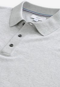 Lys grå polo-shirt lavet af blødt materiale, med krave, tre sorte knapper og en stribet detalje i nakkeområdet.