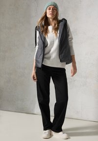 Grå puffy väst över en ljusgrå tröja, matchad med svarta vida byxor och vita sneakers. Åtföljd av en mintgrön stickad mössa.