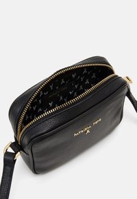Černá kožená crossbody taška se zlatými detaily, zipovým uzávěrem a vzorovaným vnitřkem s logem „Patrizia Pepe“. 