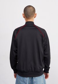 Svart sweatshirt med hög krage, med röda accentstygn, ribbade ärmslut och nederkant. Slät textur, avslappnad passform.