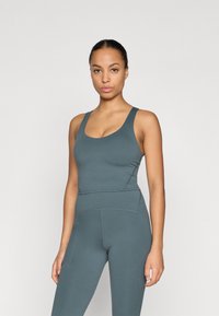 Tumši tirkīza bezšuvju sporta krūšturis un augstās vidukļa legingi, kas izceļas ar platām siksnām un pieguļošu dizainu ar smalkām šuvju detaļām.