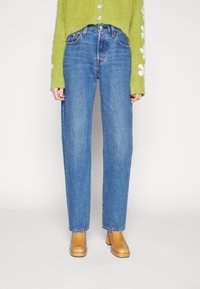 Höga blå jeans med rak skärning. Tyget har en klassisk denimtextur. Matchat med en grön fluffig kort tröja och beige klackskor.