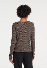 Tröja med långa ärmar i mörkbrunt med vita prickar. Har rund halsringning och en nyckelhålsdetalj bak. Mjukt, stretchigt tyg.