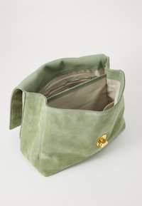 Sac à main en daim vert avec une fermeture magnétique dorée. Il dispose d'un intérieur organisé avec une poche zippée et deux compartiments ouverts.
