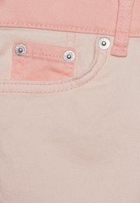 Tela de mezclilla de color rosa claro con un bolsillo que presenta herrajes de plata. Los detalles de costura son visibles, añadiendo textura al material.