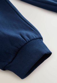 Gros plan d'une manche de sweat-shirt bleu marine avec bord-côte sur un fond clair, montrant la texture du tissu et les détails de couture.