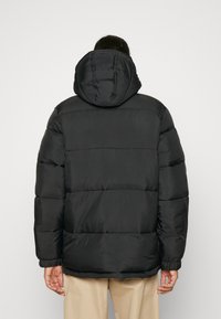 Schwarze Pufferjacke mit Kapuze, ausgestattet mit einem gesteppten Design, gerippten Bündchen und einer glatten Textur. Die Rückansicht zeigt einen lässigen Schnitt.