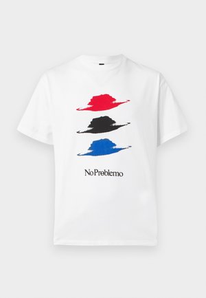 T-shirt blanc avec trois chapeaux stylisés en rouge, noir et bleu, avec le texte "No Problemo" en noir en dessous des motifs.