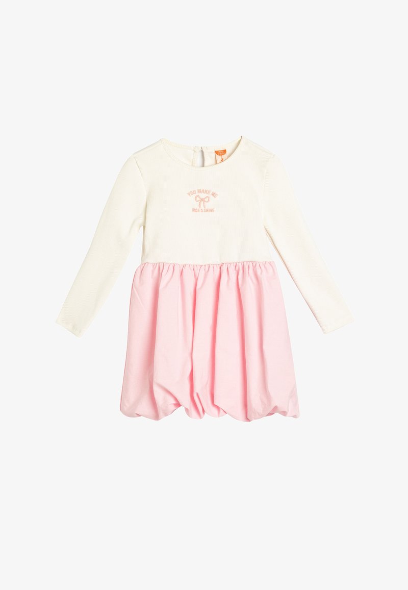 Biała sukienka z długim rękawem i różową, marszczoną spódnicą, z haftowanym napisem "Sprawiasz, że wstaję i świecę". Wykonana z miękkiej bawełny.