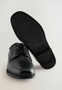 Chaussures noires en cuir avec une finition lisse, un design à lacets et une semelle plate en caoutchouc dotée de motifs de traction texturés.