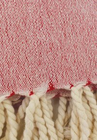 Rot-weißes gewebtes Textil mit strukturiertem Muster, ausgestattet mit cremefarbenem, gedrehtem Fransen entlang des Randes.