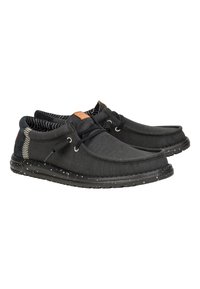 Zapatillas de lona negras con puntera redondeada, suela de goma moteada negra, forro interior a rayas y acento de cuero marrón cerca de los cordones.