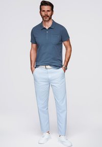 Blå polo med bröstficka, ljusblå byxor och vita sneakers. Enkel design och lätt tyg med en avslappnad passform.