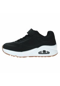 Zapato deportivo negro con una correa de Velcro, que presenta una entresuela blanca, parte superior texturizada y amortiguación de aire transparente en el talón. Suela de goma.