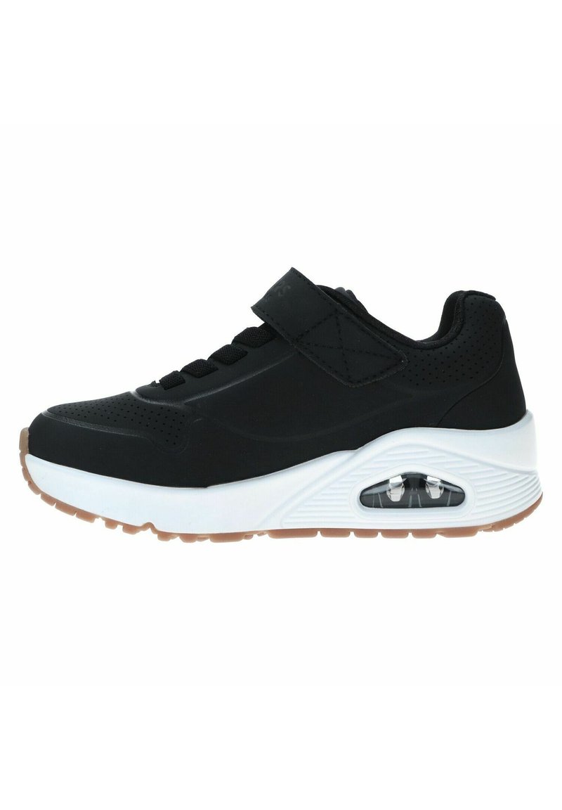 Zapato deportivo negro con una correa de Velcro, que presenta una entresuela blanca, parte superior texturizada y amortiguación de aire transparente en el talón. Suela de goma.