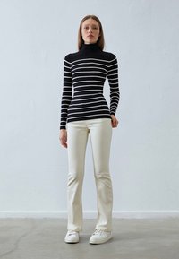Svart og hvit stripete turtleneck topp kombinert med kremfargede slim-fit bukser og hvite sneakers, satt mot en nøytral bakgrunn.