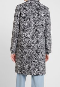 Szary wełniany płaszcz z czarnym wzorem zwierzęcym, długie rękawy i kołnierz z wycięciem, z akcentem z jednolitego szarego swetra na mankietach.