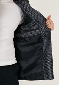 Giacca blu navy e bianca con motivo, dotata di interno in satin, tasche interne e cuciture a contrasto lungo i bordi.