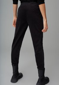 Zwarte fluwelen broeken met een tapered fit, met zijzakken en een gladde textuur. Draagt met zwarte enkelboots.
