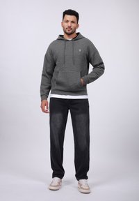 Gray textured hoodie with a kangaroo pocket and logo, paired with dark faded pants and beige sneakers. Simple and casual design.