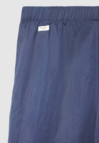 Marineblauer leichter Stoff mit einer zerknitterten Textur, ausgestattet mit einem elastischen Bund und einem Etikett mit der Aufschrift "ZERO WASTE DESIGN".