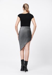 Μαύρο εφαρμοστό τοπ, ασύμμετρη ασημένια φούστα με γκλίτερ, μήκους μέχρι το γόνατο, με ομαλή υφή, συνδυασμένο με μαύρες μπότες μέχρι το γόνατο, μινιμαλιστικός σχεδιασμός.