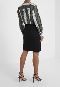 Zkrácená košile s dlouhým rukávem v zeleno-bílé pruhované vzoru; kombinována s přiléhavou černou tužkovou sukní a černými sandály na vysokém podpatku se šněrováním.