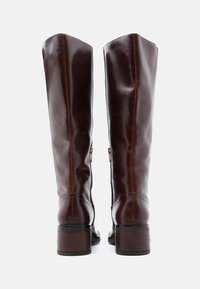 Barna bőr térd fölé érő csizmák sima textúrával, oldalsó cipzárakkal és rétegelt fából készült sarkakkal. Egyszerű, elegáns dizájnnal rendelkezik.