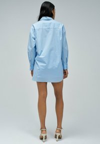 Vestido camisón de algodón suave de color azul claro y corte oversized. Presenta mangas largas, un cuello puntiagudo y un corte recto hasta la mitad del muslo.