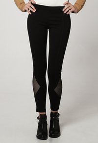 Leggings neri con un design aderente, caratterizzati da pannelli in mesh sui lati e una superficie liscia. Abbinati a stivali alla caviglia.