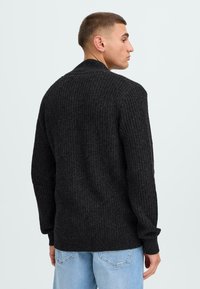 Maglione nero lavorato a maglia con una texture a coste, dotato di un collo alto e maniche lunghe, abbinato a jeans azzurri chiari.