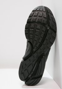 Černá sportovní podrážka obuvi s texturovaným vzorem, gumovými bloky pro záběr a drážkami pro flexibilitu.