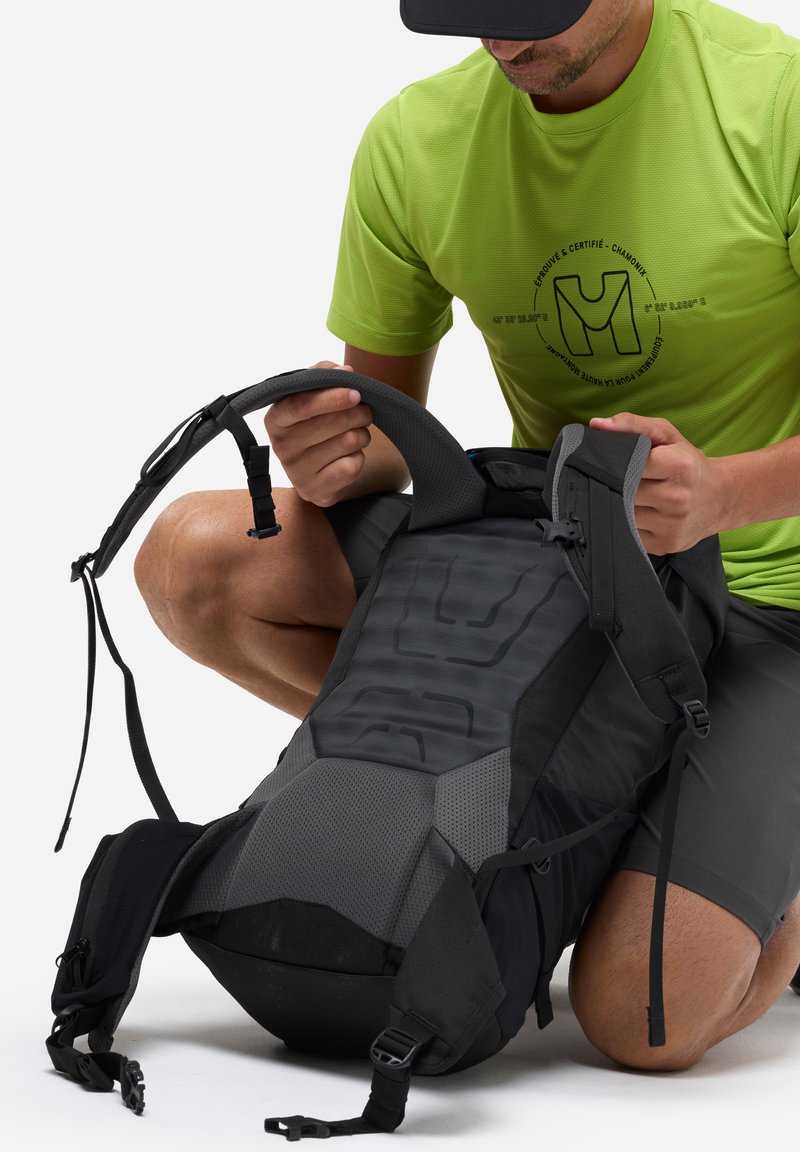 Czarny i szary plecak z teksturowanym panelem i regulowanymi paskami. Osoba bada detale paska na ramię i zapięcia.