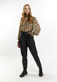 Blusa floreale marrone con collo alto e maniche voluminose, abbinata a pantaloni in pelle nera a vita alta e stivali neri con lace-up.