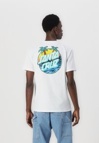 White cotton t-shirt featuring a colorful circular graphic with palm trees, waves, and "SANTA CRUZ" text on the back. Short sleeves.