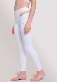 Witte leggings van rekbare stof hebben een hoge taille, uitsparingen bij de heupen en een klein merkembleem aan de zijkant.