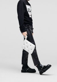 Sudadera negra con logo, pantalones de cuero negros, cartera blanca con tachuelas decorativas, botas de plataforma negras con detalles de cadena.