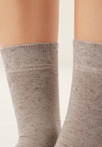 Lysegrå sokker med ribbet kant, der har en spraglet tekstur i mørkere nuancer. Materialet ser blødt og strækbart ud.