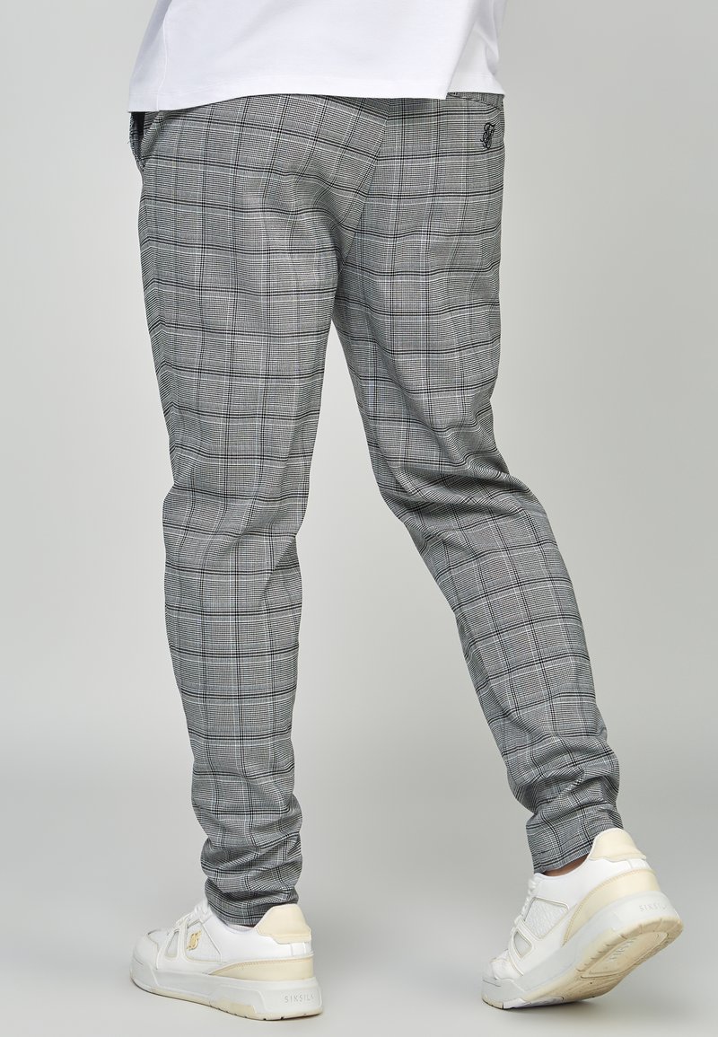 Pantaloni jogger grigi a quadri con un design aderente, caratterizzati da un motivo a scacchi discreto e un logo ricamato sul retro. Abbinati a sneakers bianche.