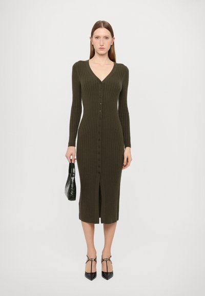 Rochie tricotată cu nervuri de culoare verde măslin, cu mâneci lungi, decolteu în V, închidere cu nasturi pe față și slit până la coapsă. Asortată cu o geantă neagră și tocuri.