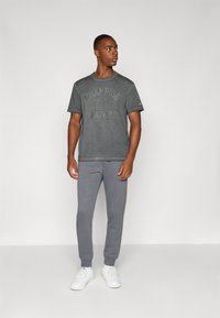 Camiseta de algodón gris con un diseño de logo descolorido, combinada con pantalones de chándal grises y zapatillas blancas. Ropa deportiva simple y casual.