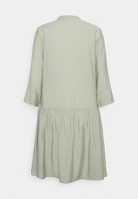 Hellgrünes, knielanges Kleid mit Rundhalsausschnitt, Dreiviertelärmeln und gerafftem Taillendetail. Glatte Textur, minimalistisches Design.