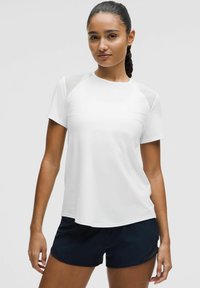 Vitt kortärmat sporttröja med rund halsringning och transparenta mesh-accenter på axlarna, matchat med svarta sportshorts.