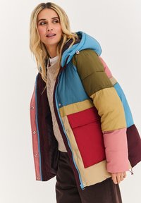 Prošívaná bunda s kapucí, která má vícebarevné panely v modré, zelené, růžové, béžové a vínové barvě. Obsahuje přední kapsu a zapínání na zip.