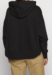 Zwarte hoodie met een relaxed fit, geribde boorden en zoom. Zachte textuur, met een grote achterzak en een minimalistisch ontwerp.