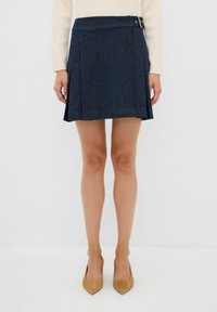 Jeanskjol i mörkblått med vertikala ränder, plisserad design och en sidobuckla som detalj. Slät textur, längd till mitten av låret.