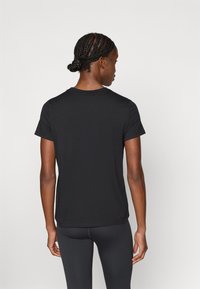 Čierne tričko, krátke rukávy, okrúhly výstrih, mäkká látka, voľný strih, zakončené rovnými lemami. Nosené s čiernymi legínami.