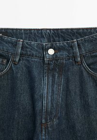 Mörkblå denimjeans med en mjuk textur, traditionell femfickdesign, knappknäppning upptill och kontrasterande sömmar.